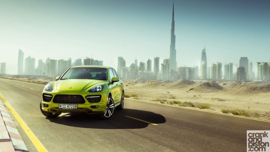 A green Porsche SUV on a deserted road with a modern city skyline and the Burj Khalifa in the background Car Hire in Dubai