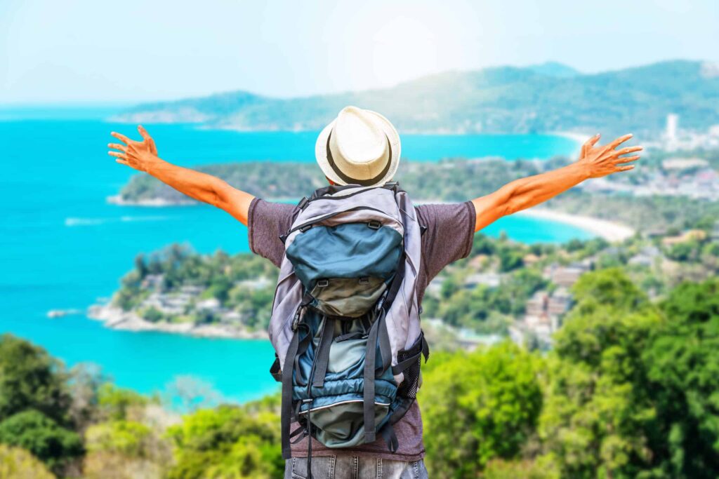 Rear view portrait of young man traveler with backpack standing on a mountain with arms spread open, Travel Life style and Adventure concept.